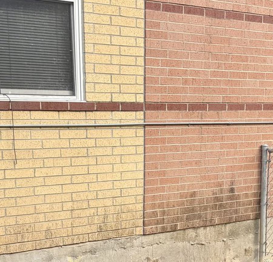 A brick school wall meeting a stained concrete foundation