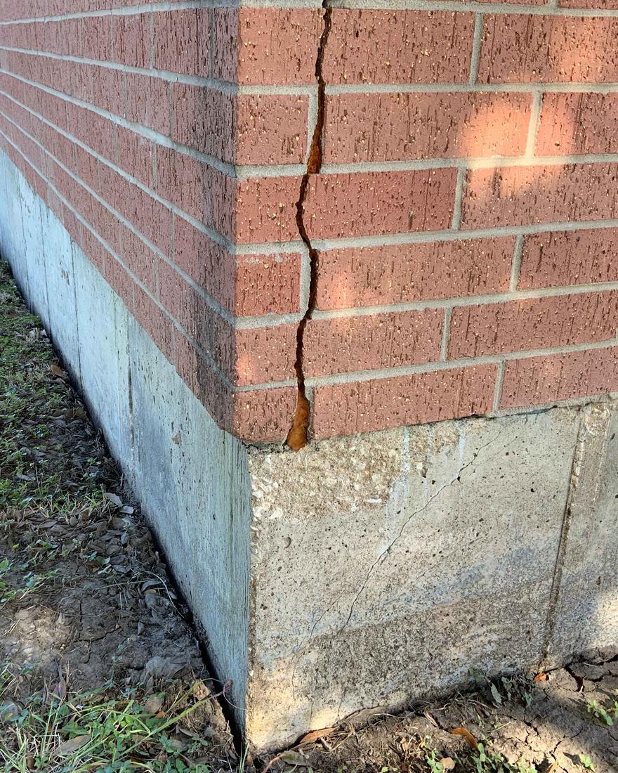 The corner of a brick school building with a crack running from the top of the wall down into the concrete foundation
