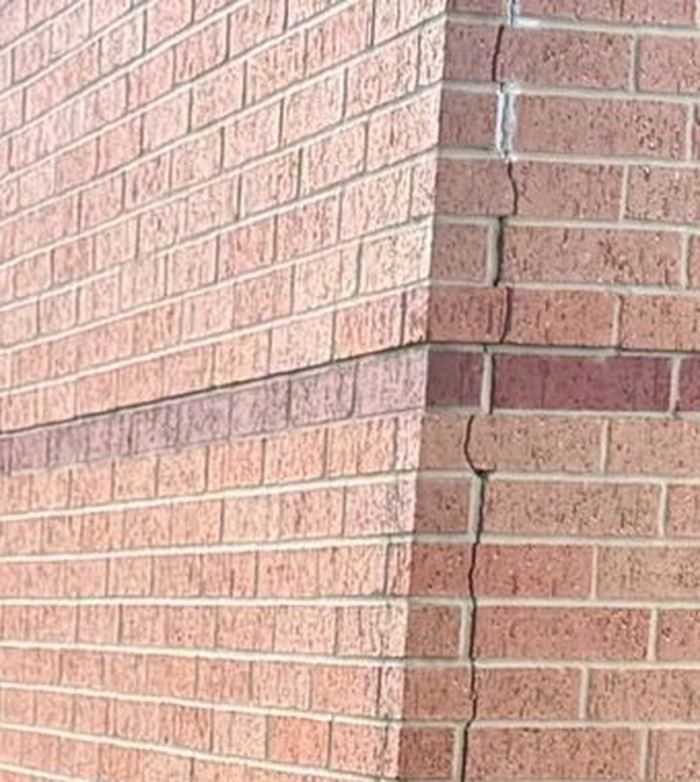 A vertical crack running down the brick corner of a school building, up close