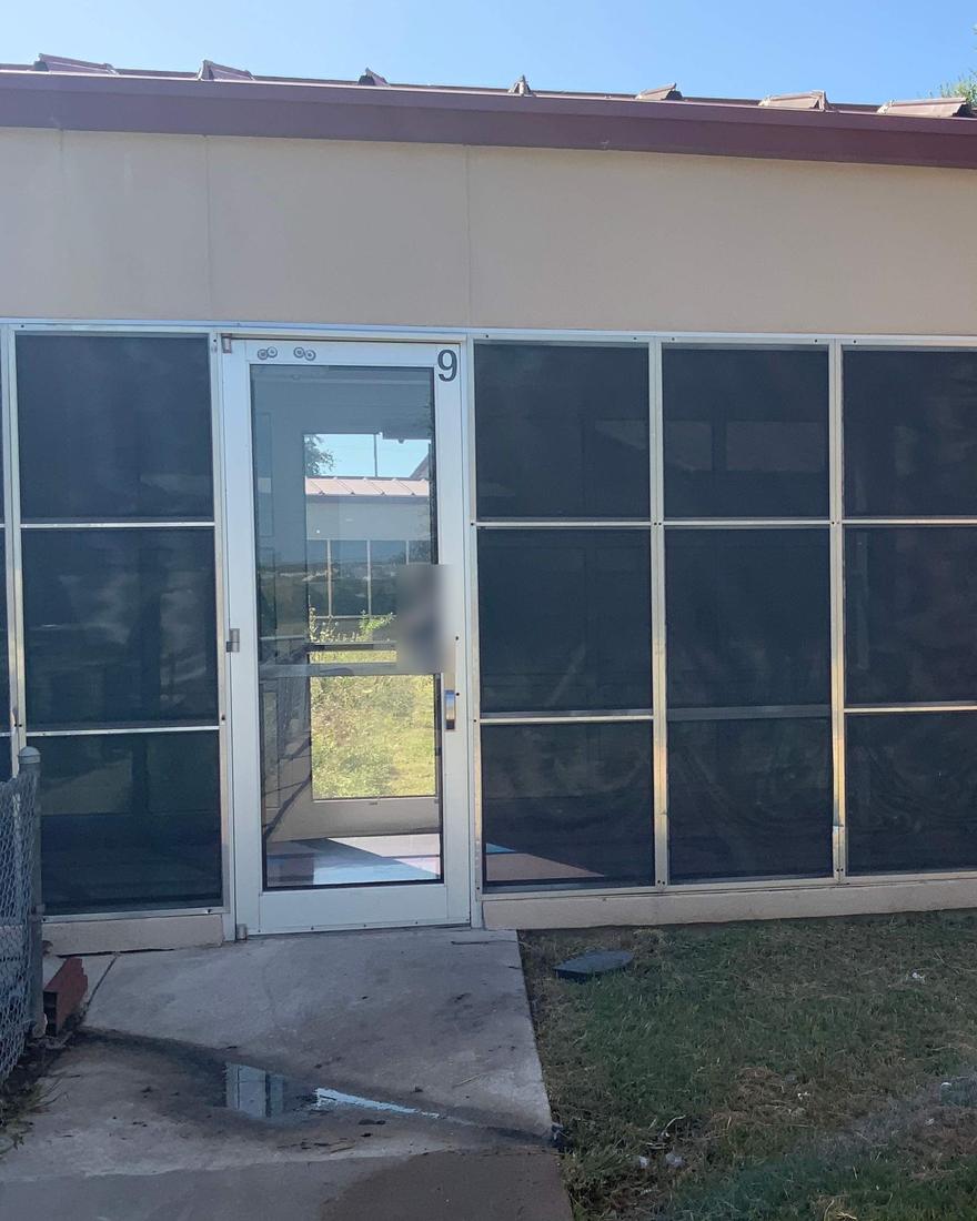 A single glass entry door numbered 9 in a wall of tinted glass, with a puddle on the concrete walk in front of it